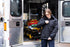 A person in tactical uniform zips up the Condor Guardian Duty Jacket | SALE while standing at the open ambulance doors, with medical equipment visible inside.
